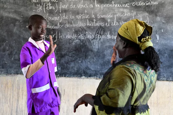 A young adolescent boy is signing against a blackboard with his teacher